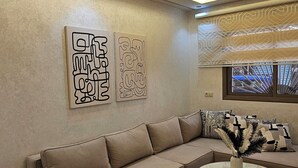 Un salon moderne avec un canapé d’angle, une table basse en verre et des œuvres d’art abstraites accrochées au mur.