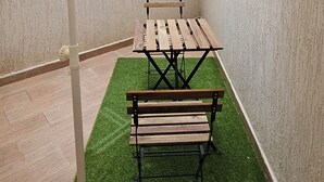 Un patio couvert avec une table et des bancs, de l’herbe artificielle et un mur blanc.