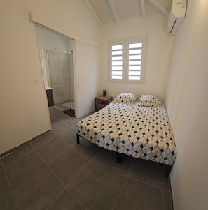 A bedroom with a bed, a window, a door, and a shower area. - Discover this pretty T3 apartment, ideal for a stay. (Sainte-Anne)