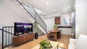 Un salon moderne avec un téléviseur à écran plat, une table basse en bois, une plante en pot et un escalier.