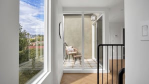 Un appartement moderne doté d'un balcon, d'une chaise en osier, d'une petite table et offrant une vue sur le paysage urbain.