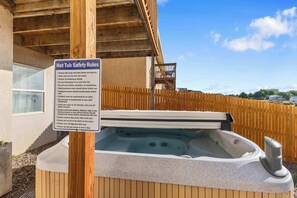 A hot tub with safety rules posted, a wooden deck, and a clear sky.