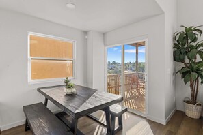 A room with a wooden table, bench, potted plant, and a sliding glass door leading to a balcony with a wooden deck.