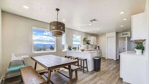 A modern kitchen with a central island, white cabinetry, and a view of the mountains through large windows. - 3BR Retreat with Hot Tub, Deck, Fire Pit,Sleeps 10 (Pueblo)