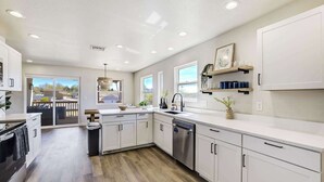 A modern kitchen with white cabinetry, a dishwasher, and a large window. - 3BR Retreat with Hot Tub, Deck, Fire Pit,Sleeps 10 (Pueblo)