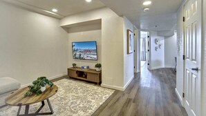 Un pasillo con piso de madera, un televisor de pantalla plana en la pared, una pequeña mesa de madera con una planta y un tapete estampado.