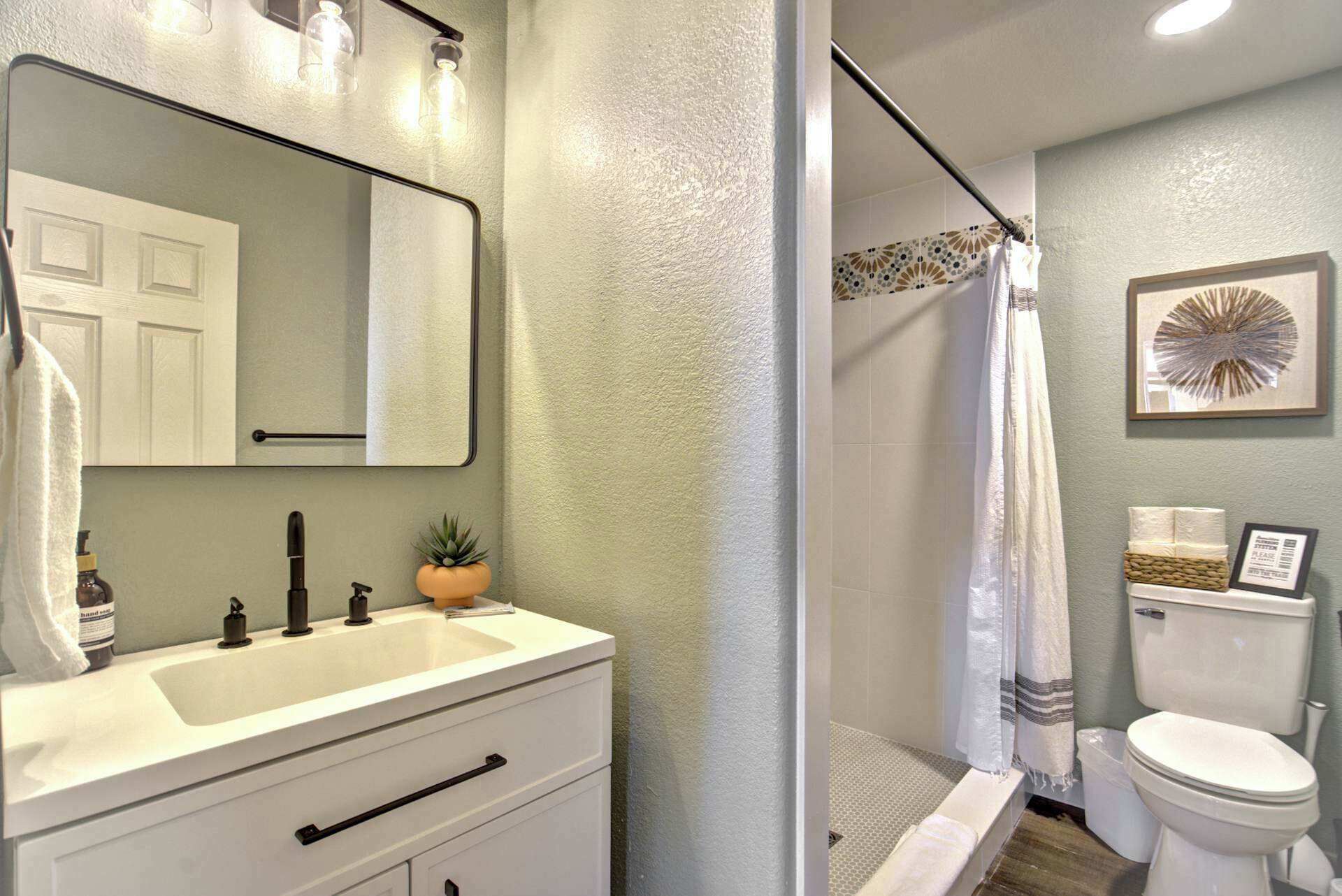 Une salle de bain avec un meuble-lavabo blanc, un miroir, un lavabo, des toilettes et un espace douche.