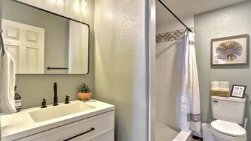 Une salle de bain avec un meuble-lavabo blanc, un miroir, un lavabo, des toilettes et un espace douche.
