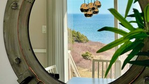 A circular mirror with a rustic design, reflecting a view of the ocean and a balcony with a hanging light fixture.