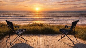 A wooden deck with two black folding chairs facing the ocean at sunset.