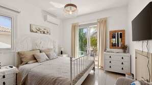 A bedroom with a bed, bedside tables, a TV, a dresser, and a balcony with curtains. - Konnos Haven Villa, Cape Greco Escape (Protaras)