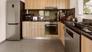 A modern kitchen with wooden cabinets, a stainless steel refrigerator, a gas stove, and a dishwasher. - Konnos Haven Villa, Cape Greco Escape (Protaras)
