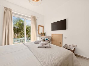 Ein Hotelzimmer mit einem großen Bett, einem an der Wand montierten Fernseher, einer Holztür und Blick ins Grüne.