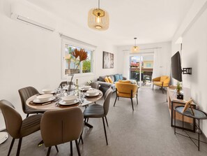 Ein modernes Wohnzimmer mit Essbereich, einer Sofagarnitur und einem an der Wand befestigten Fernseher.