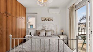 A bedroom with a bed, bedside tables, a hanging light fixture, a window, and a view of the outside. - Konnos Haven Villa, Cape Greco Escape (Protaras)