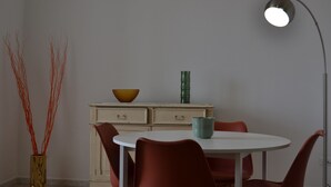 Ein Essbereich mit einem weißen Tisch, roten Stühlen, einem beigen Schrank mit Schubladen, einer grünen Vase und einer Stehlampe.