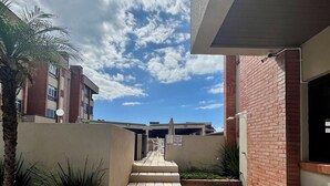 A building with a staircase leading to an entrance, surrounded by a brick wall and a palm tree. - Home office with pool and barbecue in Capão Novo - RS (Capão Novo)