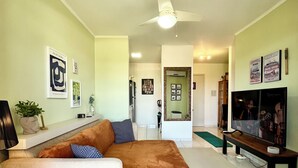 A living room with a sofa, a coffee table, a TV, and a ceiling fan. - Home office with pool and barbecue in Capão Novo - RS (Capão Novo)