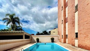 A swimming pool with lounge chairs, a tiled deck, and a brick building in the background. - Home office with pool and barbecue in Capão Novo - RS (Capão Novo)