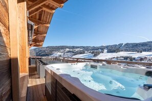 Eine Holzterrasse mit Whirlpool mit Blick auf eine verschneite Landschaft.