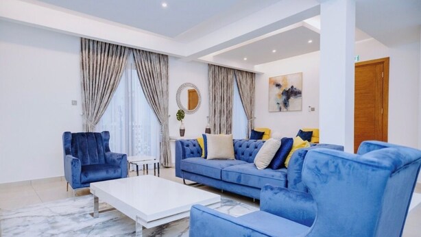 Un salon moderne avec un canapé bleu, une table basse blanche et une grande fenêtre agrémentée de rideaux.