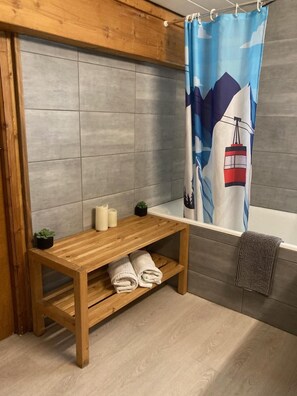 Een badkamer met een houten bankje, een handdoekrek en een douchegordijn met een berg- en kabelbaan ontwerp.