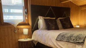 A wooden-paneled room with a bed, a small round table with a lamp, and a window with a view. - Wifi, 3rd floor, view ski slopes, balcony, parking, tv, ski locker, 70m², Les Gets (Les Gets)