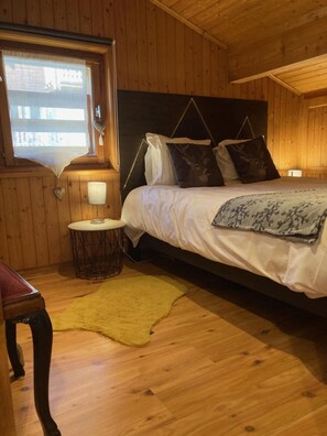 Ein Zimmer mit Holzwandverkleidung, einem Bett, einem kleinen runden Tisch mit Lampe und einem Fenster mit Blick.