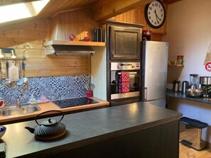 Eine Küche mit einem Edelstahl-Kühlschrank, Backofen und einer Mikrowelle. Es gibt ein Spülbecken mit Wasserhahn und einen Wasserkocher auf der Arbeitsfläche.