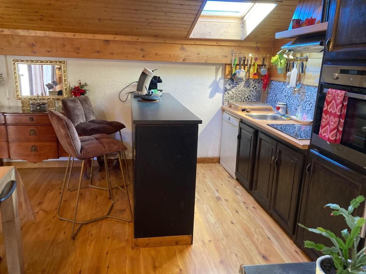 A compact kitchen with wooden flooring, a black countertop, and a small bar stool.