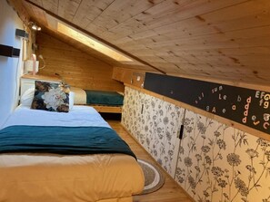 Een kamer met schuine plafonds, houten wanden, een bed met bloemenbeddengoed, een kleine tafel en een bloemen behangwand.