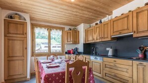 A kitchen with wooden cabinets, a dining table with chairs, and a window with a view of the outdoors. - 200m from ski slopes, 1st floor, parking, tv, ski locker, 63m², Les Gets (Les Gets)