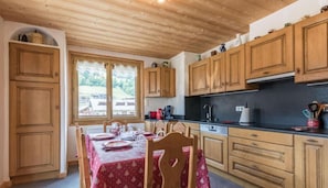 A kitchen with wooden cabinets, a dining table with chairs, and a window with a view of the outdoors. - 100m from resort center, 1st floor, parking, tv, ski locker, 63m², Les Gets (Les Gets)