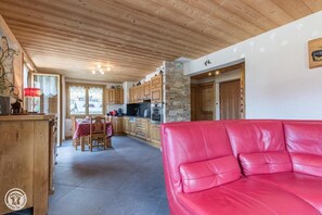 A cozy kitchen with wooden cabinets, a dining area with a table and chairs, and a red leather sofa in the living area. - 100m from resort center, 1st floor, parking, tv, ski locker, 63m², Les Gets (Les Gets)