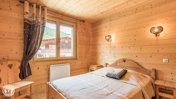 A wooden cabin bedroom with a bed, bedside tables, a window with curtains, and heart-shaped wall decorations. - 200m from ski slopes, 1st floor, parking, tv, ski locker, 63m², Les Gets (Les Gets)