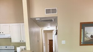 A kitchen with white cabinets, a countertop, and a stove. There are three wooden stools and a grey sofa in the living area. - Charming 2-bedroom apartment with AC in Holly Lake Ranch (Holly Lake Ranch)