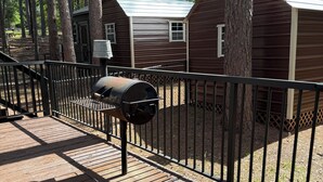 A wooden deck with a grill, metal fence, and cabins in a wooded area. - Charming 2-bedroom apartment with AC in Holly Lake Ranch (Holly Lake Ranch)