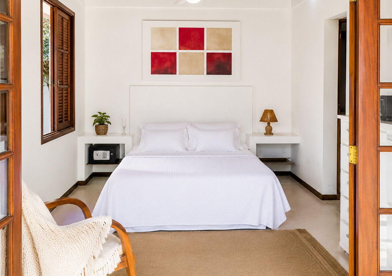 Un dormitorio con cama, mesitas de noche, lámpara, planta y ventana con persianas de madera.