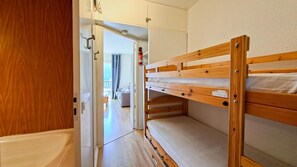 Ein Schlafzimmer mit Etagenbetten, einer Holztür, einem sichtbaren Badezimmer und Blick in einen weiteren Raum mit einem Sofa.