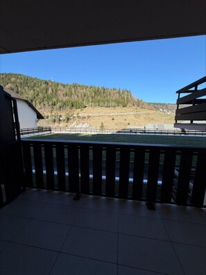 Ein Balkon mit Blick auf einen bewaldeten Hügel und ein Gebäude in der Ferne.