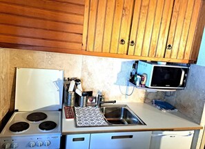 A compact kitchen with a stove, sink, microwave, and wooden cabinets. - 100m from resort center, 1st floor, balcony, tv, ski locker, 25m², Pra Loup (Pra Loup)