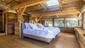 Une chambre spacieuse avec un grand lit, des poutres apparentes et des fenêtres de toit.