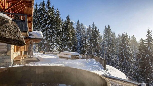 Une cabane en bois avec un bain à remous, entourée d’arbres couverts de neige et sous un ciel dégagé.