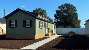 A green building with a porch, a small table and chair, and a clear sky.
