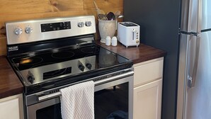 A kitchen with a stainless steel stove, a refrigerator, wooden shelves with kitchenware, and a wall clock.