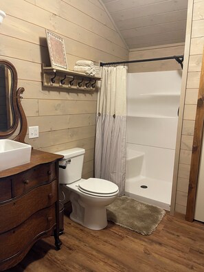 Ein Badezimmer mit einem Holzkosmetikschrank, einer Toilette, einer Dusche mit gestreifter Duschvorhang und einem Holzbodenregal mit Handtüchern.