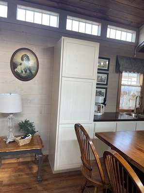 Une cuisine avec une table en bois, des chaises, un réfrigérateur et une fenêtre avec des rideaux.