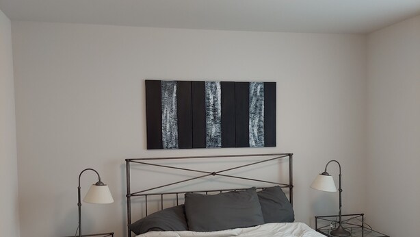 Een slaapkamer met een bed, twee nachtkastjes, een plafondlamp en een kunstwerk aan de muur.
