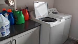 Een wasruimte met een wasmachine, wasmiddel en een spiegel.