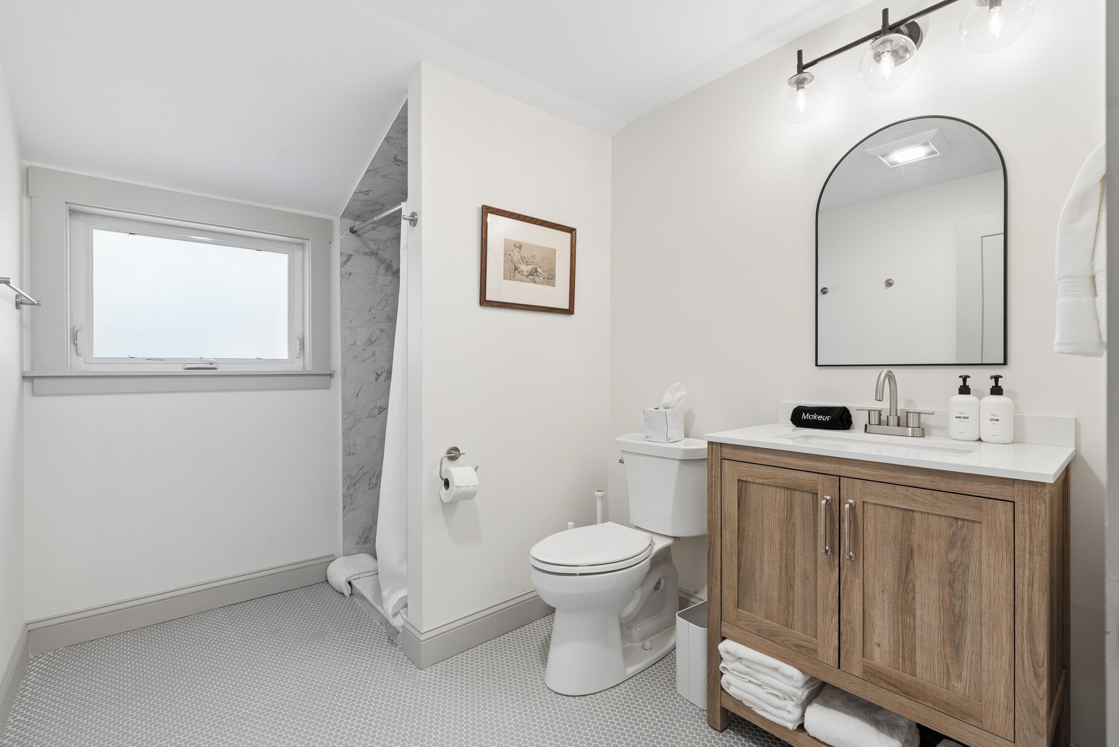 A bathroom with a toilet, a sink with a mirror, a shower, and a window.